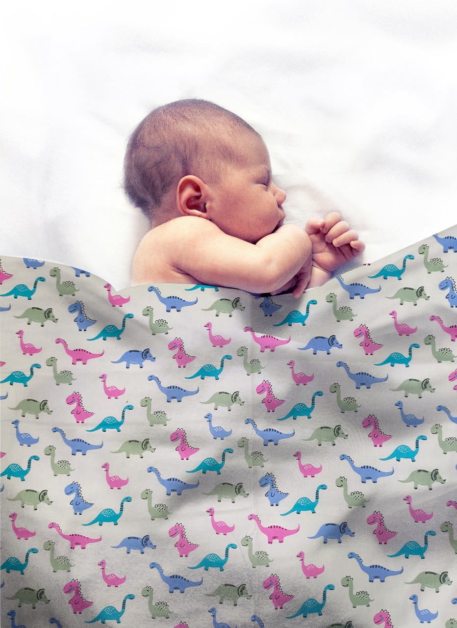 Newborn baby sleeping under a colorful dinosaur-patterned blanket on a white background